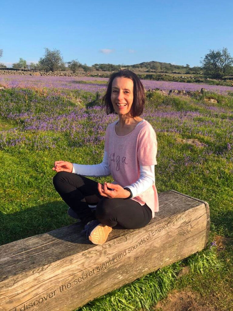 Photo of Sarah sat on a bench with bluebells in the background